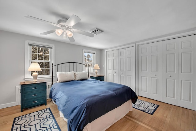 bedroom featuring ceiling fan, two closets, and light wood-type flooring