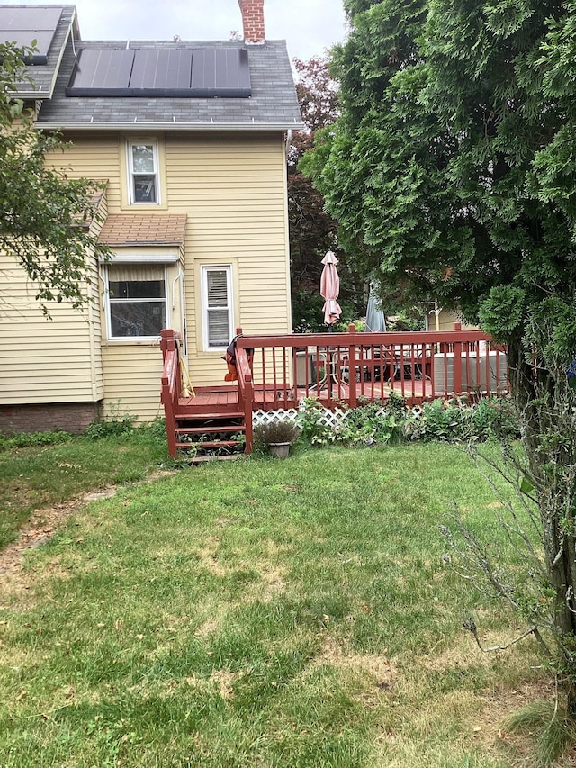 back of house with a chimney, a deck, and a lawn
