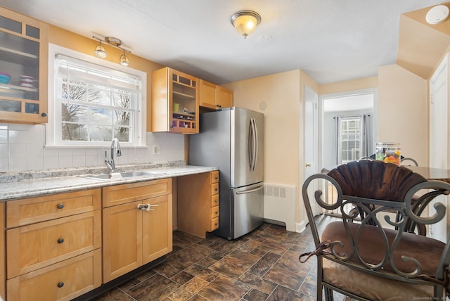 kitchen featuring radiator heating unit, stainless steel refrigerator, light brown cabinetry, sink, and backsplash