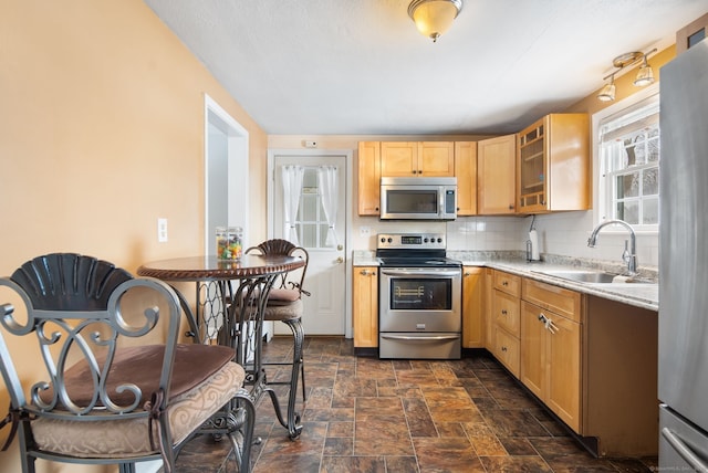 kitchen with sink, appliances with stainless steel finishes, light stone counters, tasteful backsplash, and light brown cabinetry