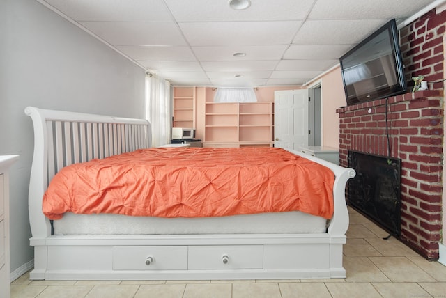 bedroom with a brick fireplace, light tile patterned floors, and a drop ceiling