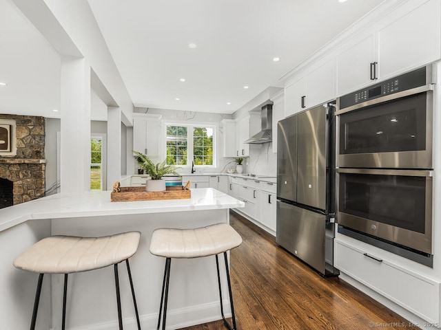 kitchen featuring a breakfast bar area, stainless steel appliances, tasteful backsplash, white cabinets, and wall chimney exhaust hood