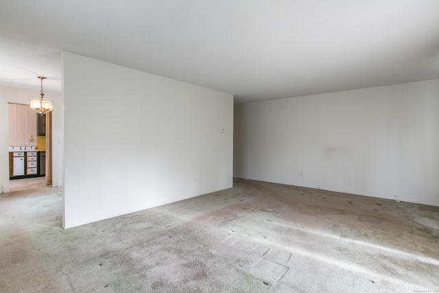 spare room featuring an inviting chandelier and light colored carpet