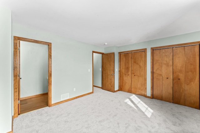 unfurnished bedroom featuring light colored carpet and two closets