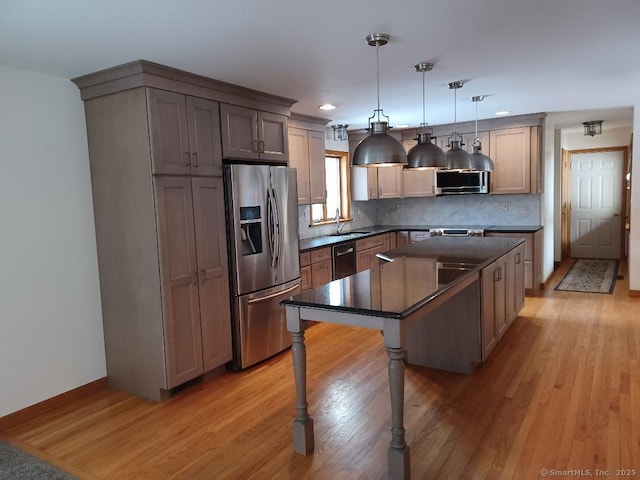 kitchen with a kitchen island, appliances with stainless steel finishes, decorative light fixtures, sink, and light wood-type flooring