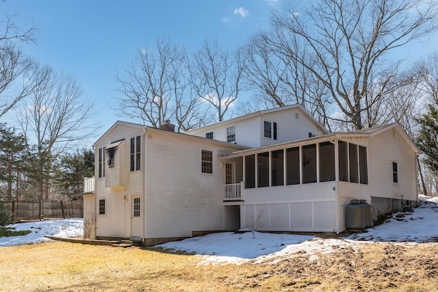 snow covered property featuring a chimney, fence, and a sunroom