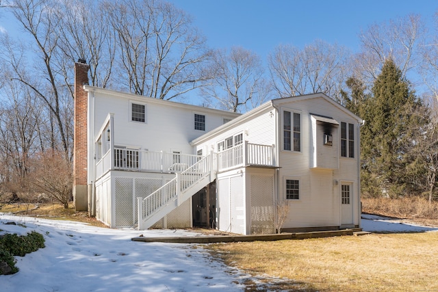 snow covered back of property with stairs, a deck, and a chimney