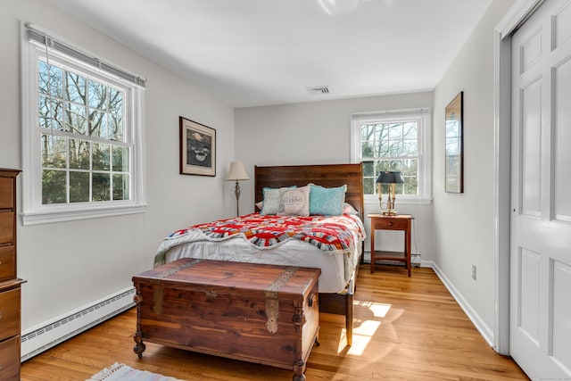 bedroom with a baseboard heating unit, multiple windows, light wood-type flooring, and baseboards