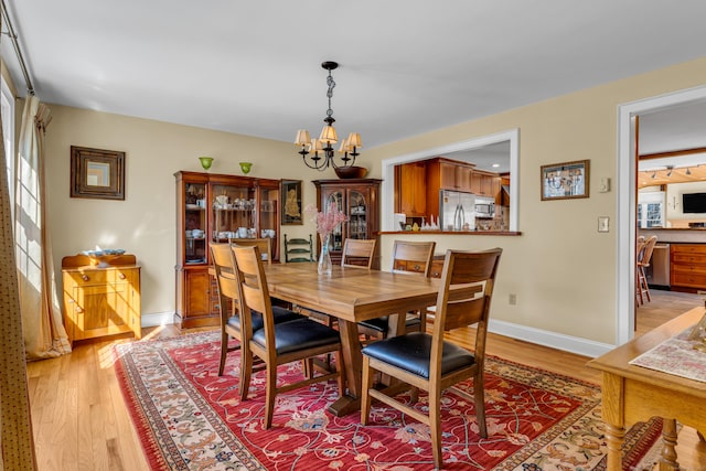 dining room featuring light wood-type flooring, baseboards, and a notable chandelier