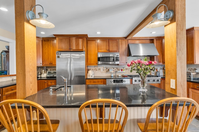 kitchen featuring stainless steel appliances, a kitchen breakfast bar, wall chimney range hood, tasteful backsplash, and brown cabinetry