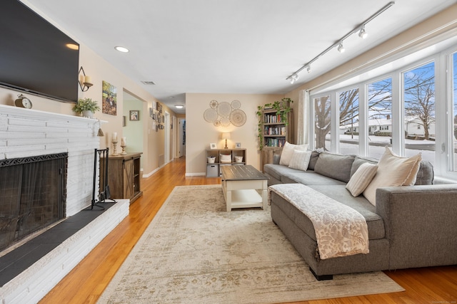 living room with a brick fireplace, track lighting, and light hardwood / wood-style flooring