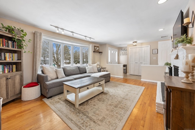 living room featuring a brick fireplace, track lighting, and light wood-type flooring