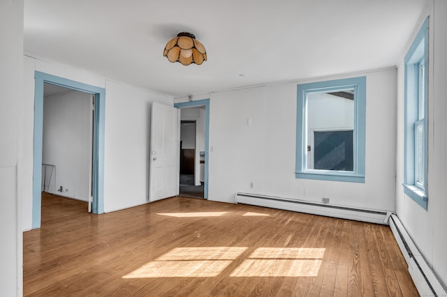 spare room with plenty of natural light, wood finished floors, baseboard heating, and a baseboard radiator