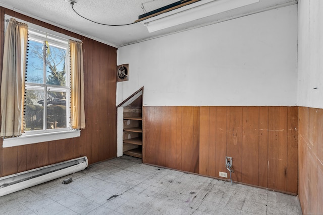 empty room with tile patterned floors, baseboard heating, wood walls, and a textured ceiling