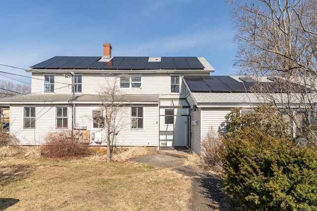 rear view of house with a yard, roof with shingles, solar panels, and a chimney