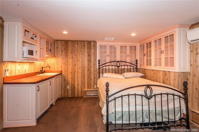 bedroom with dark wood-type flooring, a wall mounted air conditioner, wooden walls, and sink