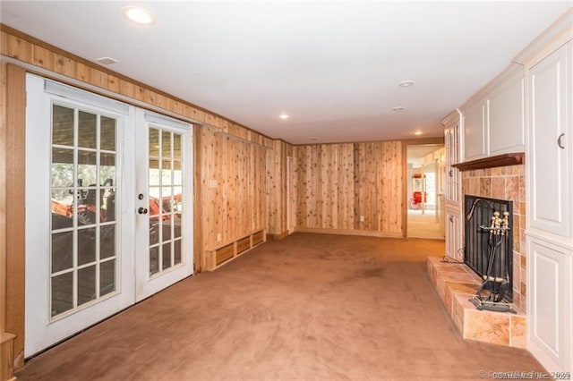 unfurnished living room featuring light carpet, wooden walls, and french doors