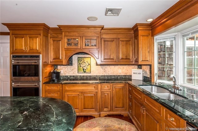 kitchen featuring sink, black electric cooktop, double oven, dark stone counters, and backsplash