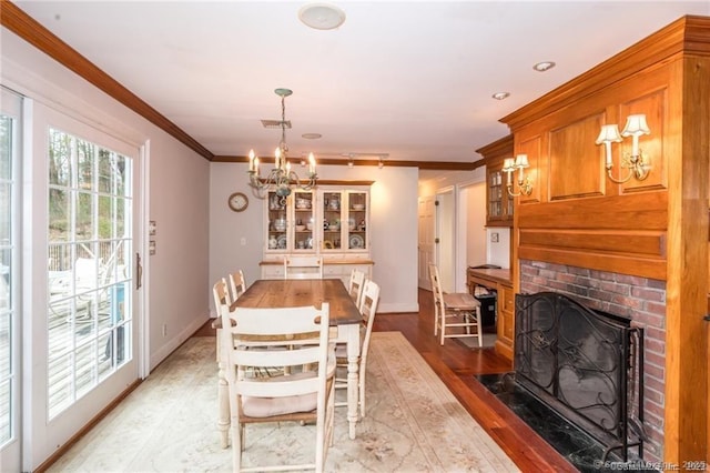 dining room featuring crown molding, a fireplace, an inviting chandelier, and light wood-type flooring