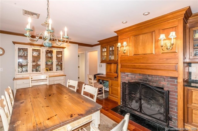 dining area featuring an inviting chandelier, crown molding, a fireplace, and dark hardwood / wood-style floors