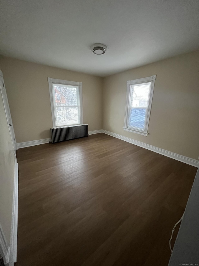 empty room with radiator heating unit and dark hardwood / wood-style flooring