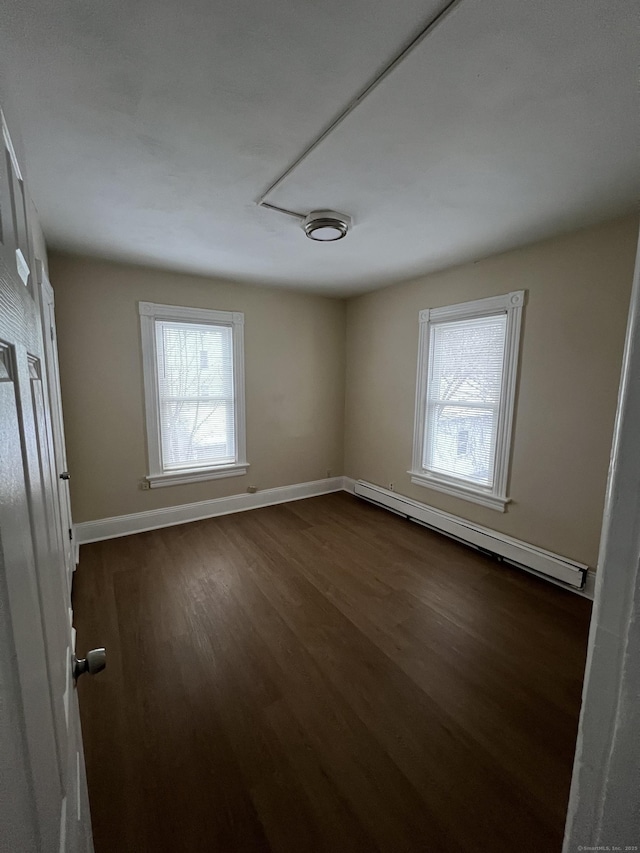 empty room with baseboard heating and dark hardwood / wood-style flooring