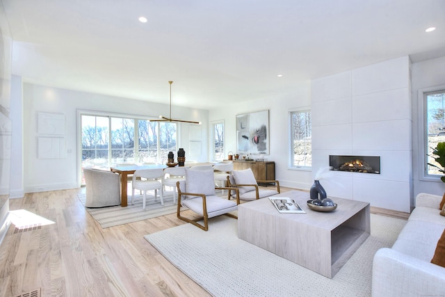 living room featuring recessed lighting, a large fireplace, light wood-style flooring, and baseboards