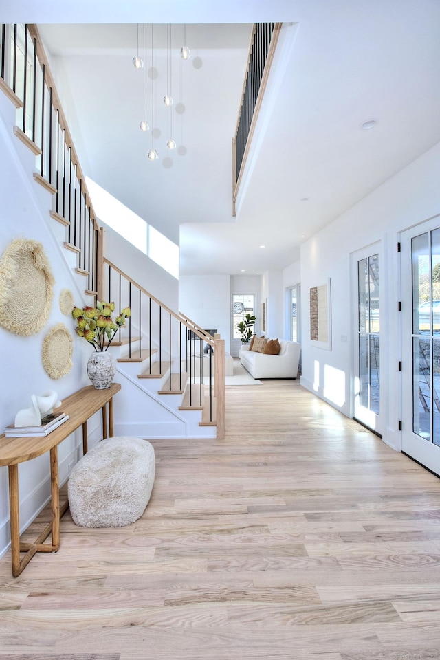 foyer entrance with baseboards, a towering ceiling, light wood-style flooring, stairs, and recessed lighting