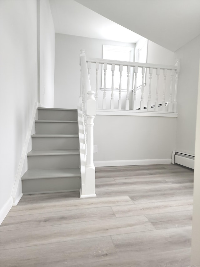 stairway featuring baseboards, a baseboard heating unit, and wood finished floors