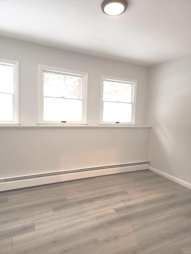 spare room with baseboards, a baseboard radiator, and wood finished floors
