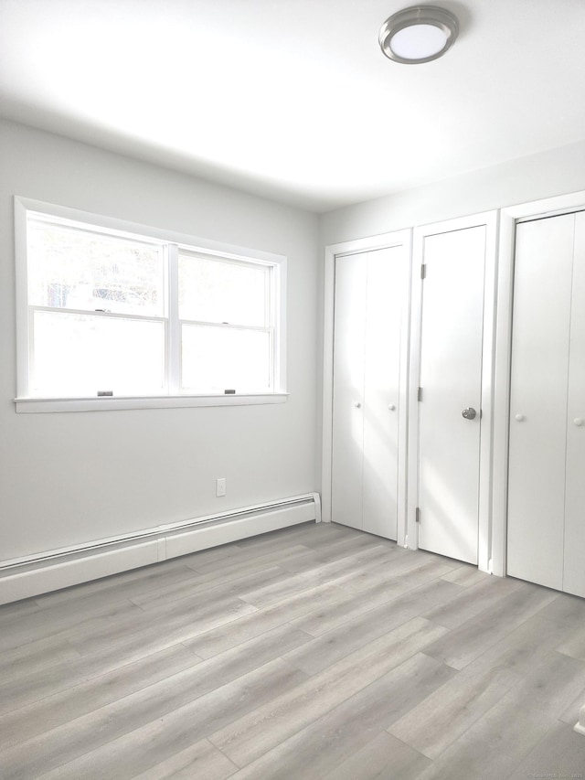 unfurnished bedroom featuring baseboard heating, two closets, and light wood-type flooring