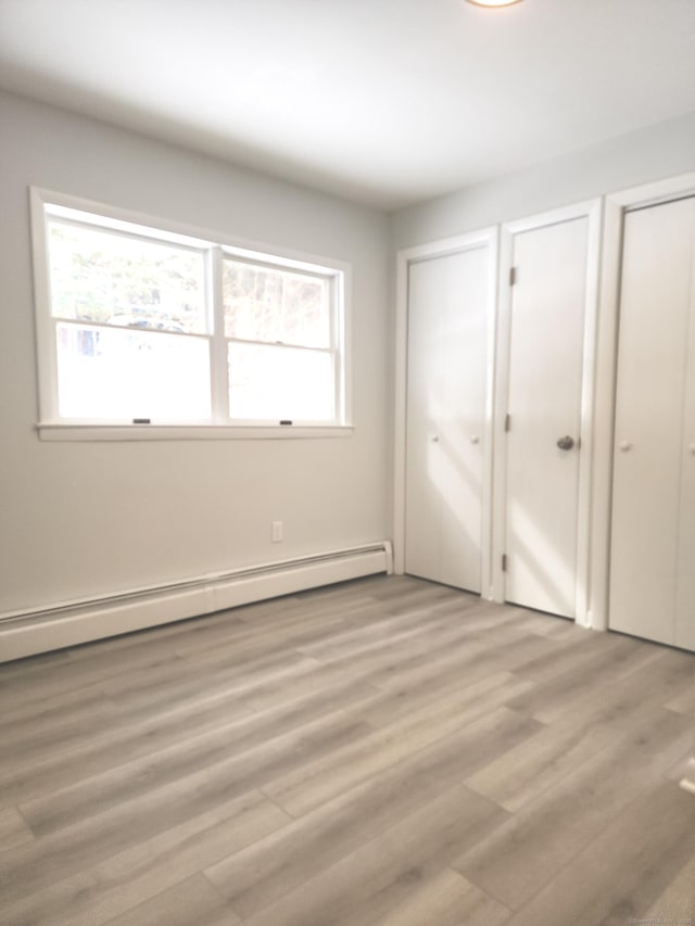 unfurnished bedroom featuring light wood-type flooring, a baseboard heating unit, and two closets
