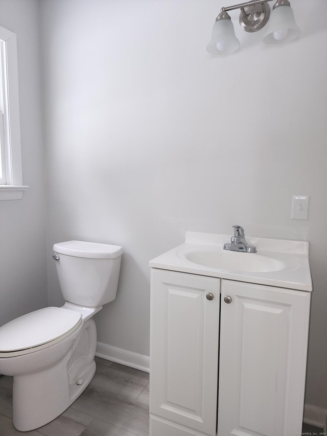 bathroom featuring toilet, baseboards, wood finished floors, and vanity