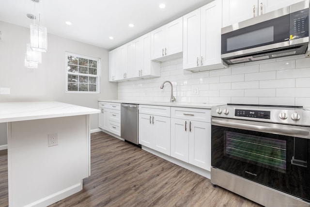 kitchen featuring stainless steel appliances, light stone countertops, white cabinets, decorative light fixtures, and sink