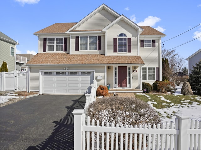 traditional home featuring a garage, fence private yard, aphalt driveway, and roof with shingles