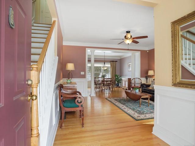 foyer entrance featuring light wood-type flooring, a wainscoted wall, stairs, and ornate columns