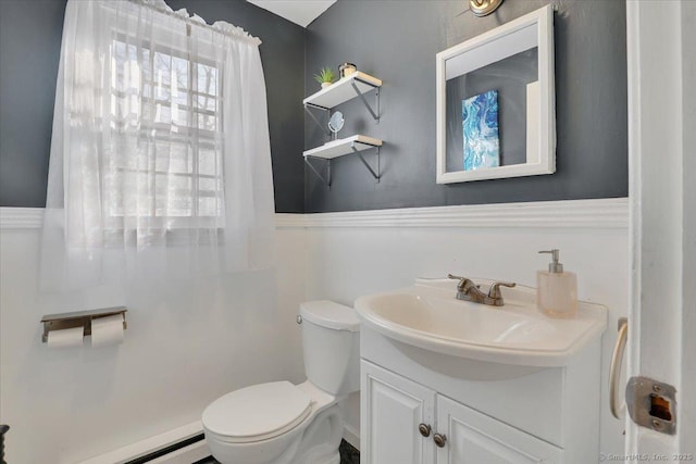 half bath with a baseboard heating unit, vanity, and toilet