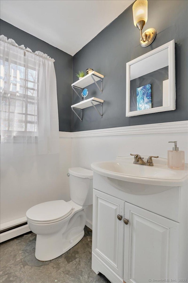 half bathroom featuring toilet, baseboard heating, and vanity