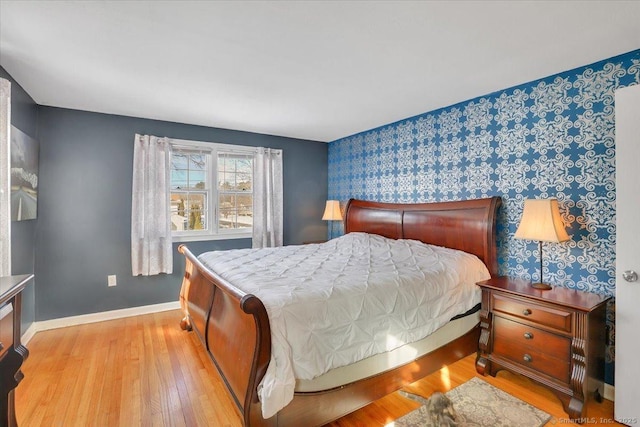 bedroom with baseboards, an accent wall, light wood-type flooring, and wallpapered walls