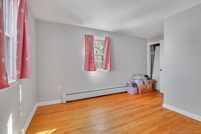 empty room featuring a baseboard heating unit, light wood-type flooring, and baseboards