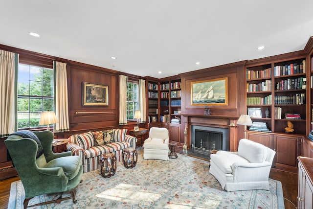 sitting room with built in shelves, recessed lighting, dark wood-style flooring, a fireplace with flush hearth, and ornamental molding