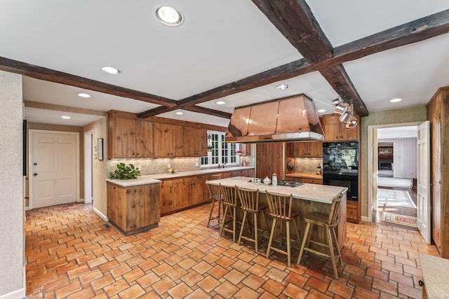 kitchen featuring a breakfast bar area, dobule oven black, island range hood, light countertops, and a center island