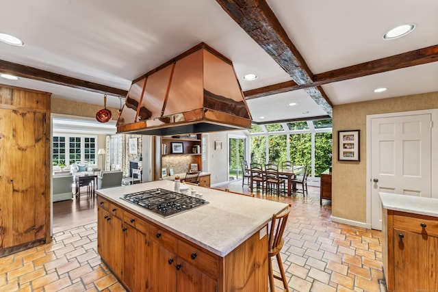 kitchen featuring a center island, stainless steel gas cooktop, light countertops, decorative backsplash, and baseboards