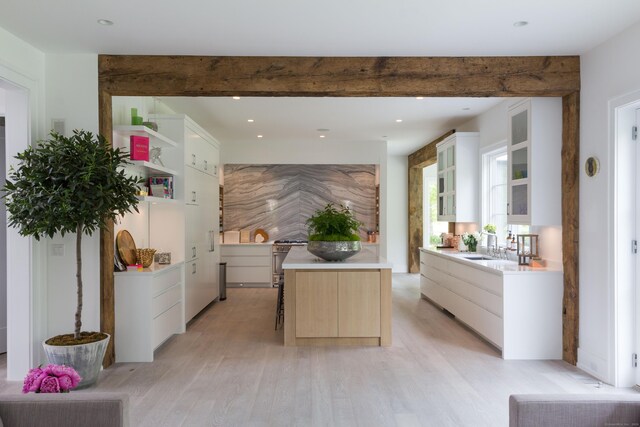 kitchen with light wood finished floors, glass insert cabinets, a center island, light countertops, and beam ceiling