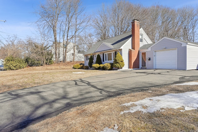 view of front of property featuring an attached garage, driveway, a chimney, and a shingled roof