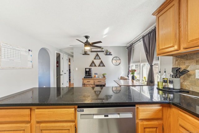 kitchen with tasteful backsplash, arched walkways, dark stone counters, dishwasher, and ceiling fan