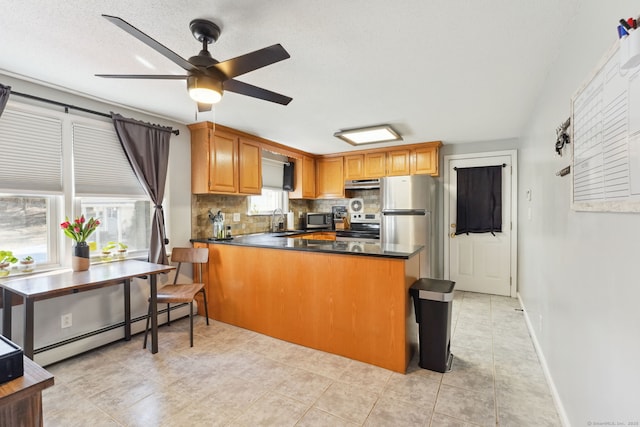 kitchen featuring a baseboard heating unit, stainless steel appliances, a peninsula, a sink, and tasteful backsplash