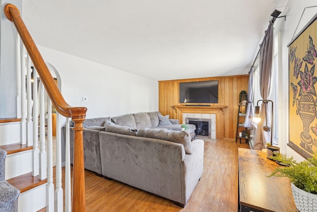 living room with a tiled fireplace, stairway, light wood-type flooring, and wooden walls