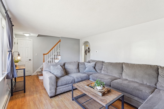 living room with arched walkways, a textured ceiling, a baseboard heating unit, light wood-style floors, and stairway