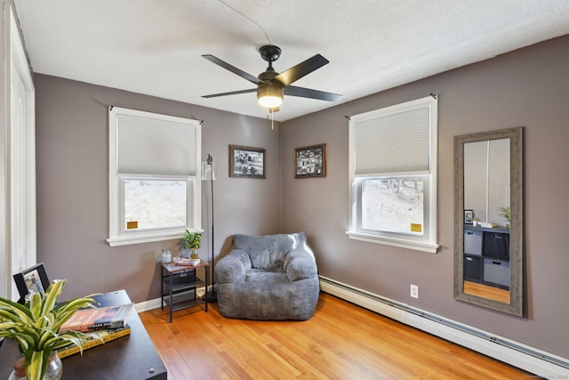 sitting room with wood-type flooring, baseboards, plenty of natural light, and baseboard heating